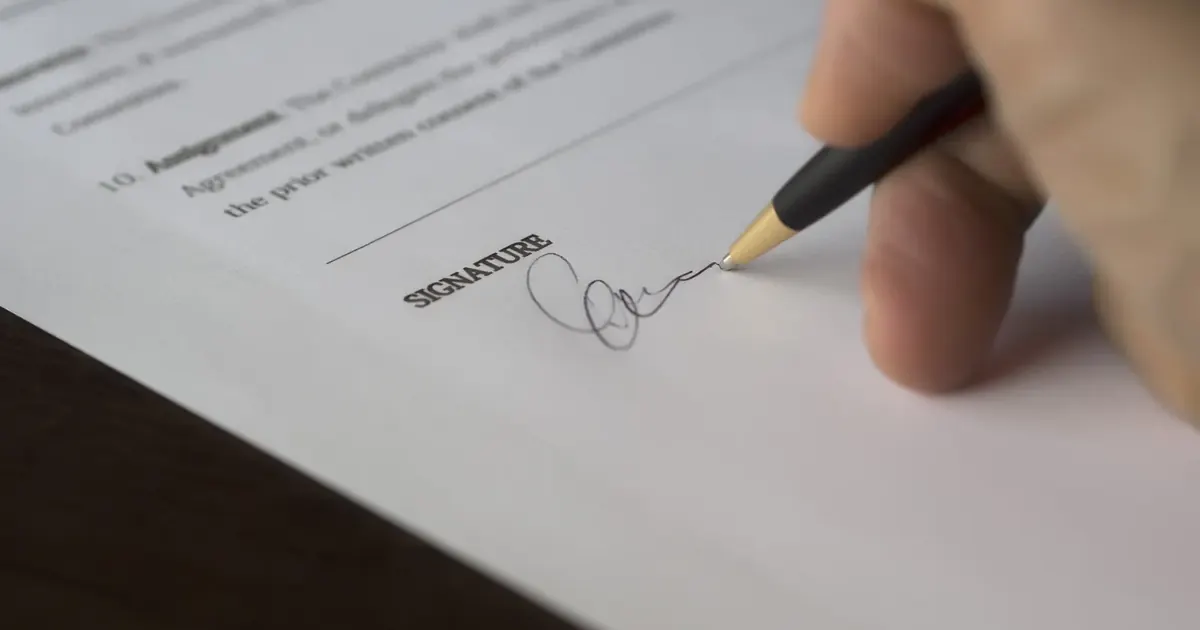 Promesa de compraventa vs escritura pública en Colombia Persona firmando un contrato con bolígrafo sobre la línea de la firma — promesa de compraventa vs escritura en Colombia